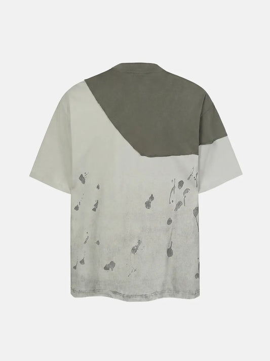 DistopionのFacade Splatter Teeのバックビュー。右肩から背中にかけて斜めに大胆に切り替えられたダークトーンの切りっぱなしパネルと、背面下部に広がるインクスプラッターグラフィック、リラックス感のあるドロップショルダーのシルエット。