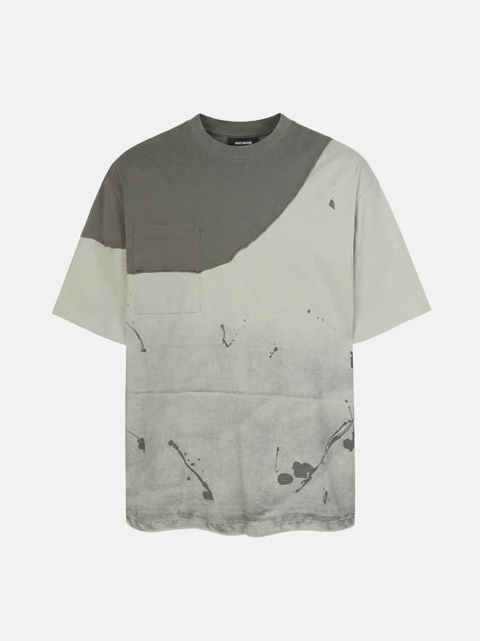 DistopionのFacade Splatter Tee。ウォッシュ加工が施されたライトグレー系のボディに、ダークトーンの切りっぱなしアシンメトリー胸パネルと同系色ポケット、全体に飛び散るような黒のインクスプラッターグラフィックがあしらわれた超厚手オーバーサイズTシャツ。