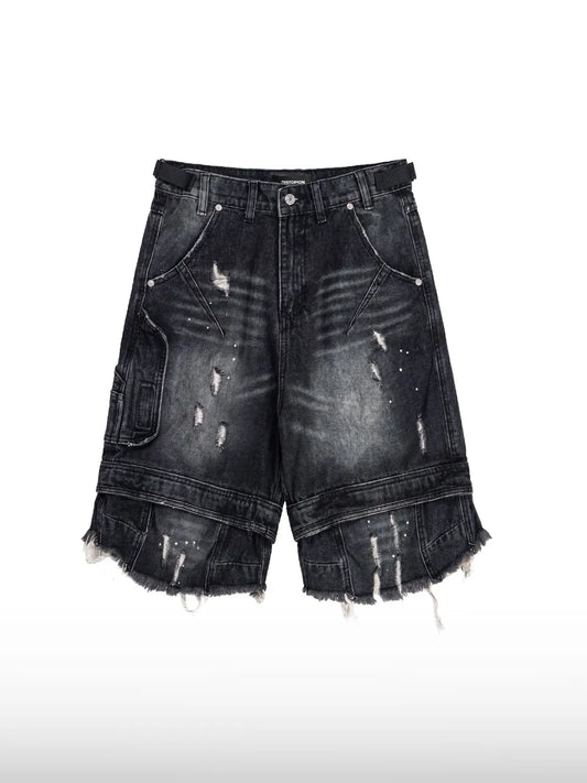 DistopionのGrunge Denim Shortsのフロントフラットレイ画像。ウォッシュ加工された黒デニムにスクラッチダメージと白ペイントが散りばめられ、ウエストに黒のアジャスターベルト、裾が二重構造の切りっぱなしになったワイドショーツ。