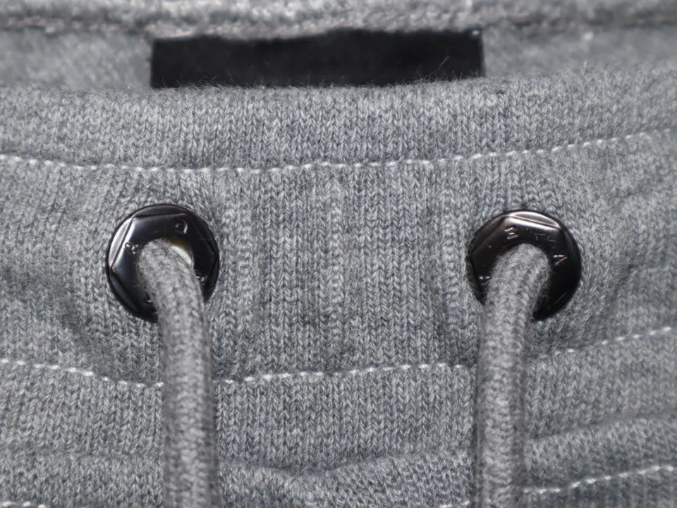 Layered Sweat Pants MADFRENZYのウエストハトメ部分アップ画像。ブランドロゴが彫り込まれたナット風のブラックメタルハトメ金具。
