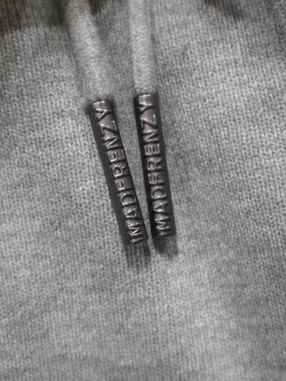 【MADFRENZY】 Layered Sweat Pants ブランドロゴ刻印ドローコードチップ画像。「MADFRENZY」ロゴが刻印されたブラックメタルのドローコードチップ。