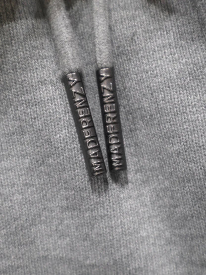 【MADFRENZY】 Layered Sweat Pants ブランドロゴ刻印ドローコードチップ画像。「MADFRENZY」ロゴが刻印されたブラックメタルのドローコードチップ。