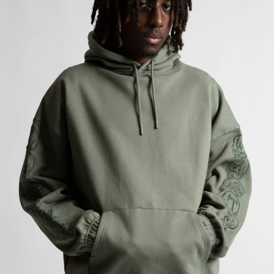 【WASTED PARIS】 BURY BOXY HOODIE （KAHKI） 両袖の連続刺繍ディテールを強調した男性モデルのアップ画像